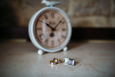 Wedding accessories. Gold rings and cufflinks on white textured table and clock on the backgroundの写真素材