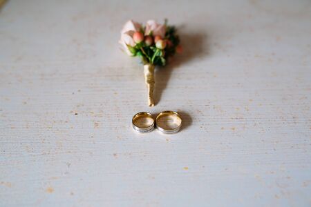 Wedding accessories. Boutonniere, Golden rings, a beautiful bouquet of flowers on white textured table. Concept of bride and groom ornamentationの写真素材