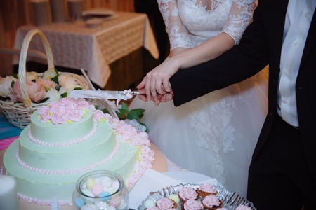 Close-up Hands of the bride and groom cut the wedding cake. Concept of candy shopの写真素材