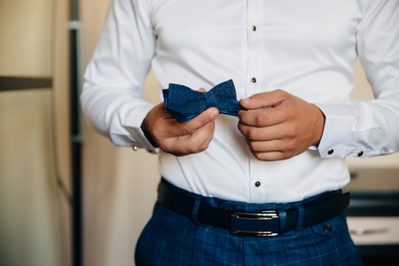 Close-up businessman groom holding bow-tie in his hands. Concept of men stylish elegance clothesの写真素材