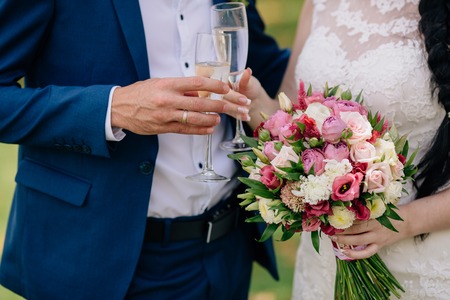 Closeup groom and bride are holding hands with a glass of champagne at wedding day and show rings. Concept of love familyの写真素材