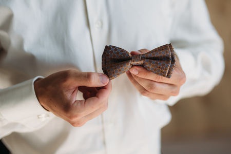 Closeup Groom hands with bow-tie. Elegant gentleman clother, white shirt and brown beltの写真素材