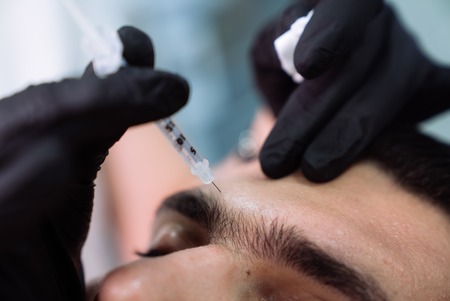 Close up male patient face and cosmetologists hands with syringe during facial beauty injections.の写真素材