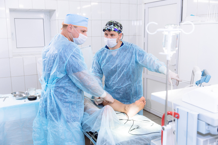 A team of doctors in sterile medical gowns perform surgery in a surgical room. The surgeon shows the diagnostic equipment and communicates with the assistant.の写真素材