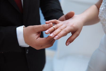 Close-up of the hands of men and women who are getting married. A man puts on a wedding ring on a slender, graceful finger of a girl.の写真素材