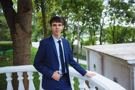 A young married man in a strict blue suit is posing on a large balcony overlooking the park on her wedding day. An agitated young man.の写真素材