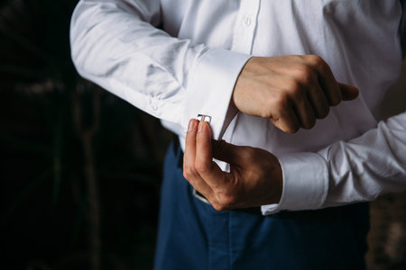Close-up groom hands hold cufflinks. Elegant gentleman clother, white shirt and black belt. concept...