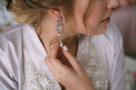 Close-up earrind in the hands of the bride on her ear. Concept of jewelry. Morning preparation of the bride for marriage.の写真素材