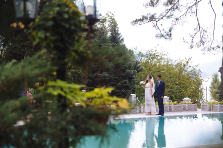 Silhouettes of the newlyweds are reflected in the water, the couple are strolling along the green territory of the hotel, admiring the nature.の写真素材
