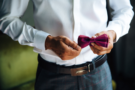 Close-up of a cropped frame of a stylish business man going to a wedding. A businessman in a snow-white shirt dresses a bow tie, wears a fashionable suit, a leather belt.の写真素材