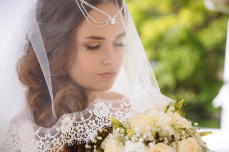 A close-up of a young bride has closed her eyes from feelings overwhelming her, is preparing to enter the church, put on a veil and closed her face.の写真素材
