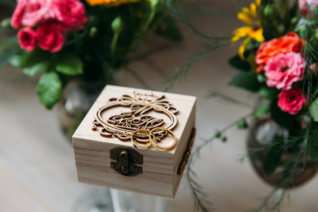 A close-up of the gold wedding rings rests on a wooden box with engraved names of the newlyweds, against the background of bright colors in vasesの写真素材
