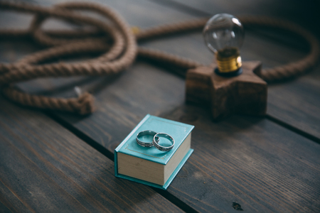 Gold wedding rings lie on a blue gift box on a brown wooden retro table. Decoration with electric lamp, rope. The concept of jewelry.の写真素材