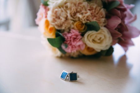 Close-up a cufflinks and a wedding bouquet on a white table. Clothing accessories for businessman or groomの写真素材