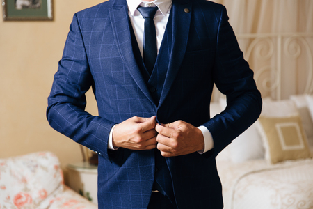 Close-up of a cropped frame of a business stylish man buttoning his jacket, standing in a stylish office with designer repairの写真素材
