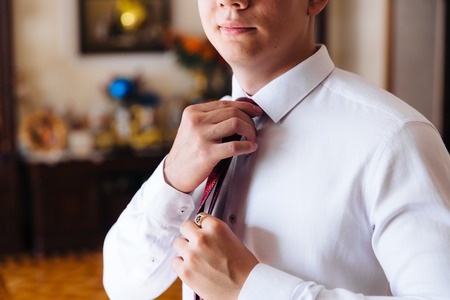 Close-up of a cropped frame of a slender business man in a trendy suit wearing dark trousers and a white shirt is holding a tie in his hands. A businessman is going to try on a red tie.の写真素材