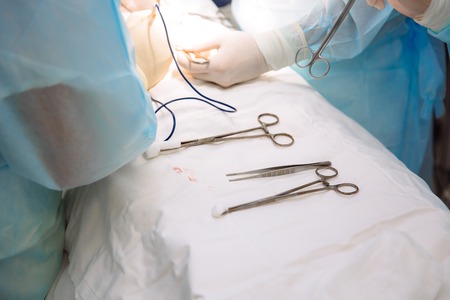 Close-up surgical instruments on a medical table in a clinic during surgery. Metal sterile scissors, clamp, surgical needle at the table or in doctor hand. The concept of health, tools.の写真素材