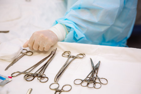 Close-up surgical instruments on a medical table in a clinic during surgery. Metal sterile scissors, clamp, surgical needle at the table or in doctor hand. The concept of health, tools.の写真素材