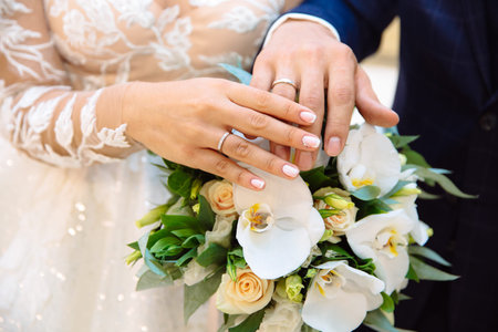 Close-up of the hands of the newlyweds with wedding rings, gently touch the wedding bouquet of...