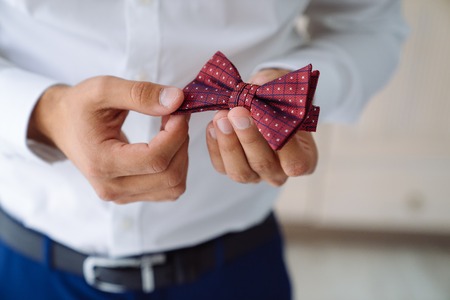 Close-up businessman hold bow tie in hands, wears a fashionable suit, a leather belt. Preparation of groom for wedding day.の写真素材