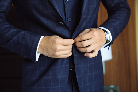 Close-up business stylish man buttoning his jacket, standing in a stylish office with designer repair.の写真素材
