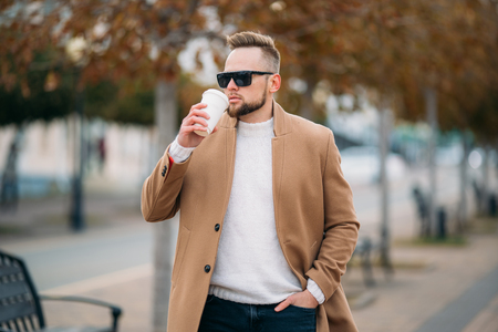 Handsome bearded young man in sunglasses drinking coffee in park, copy space on cupの写真素材