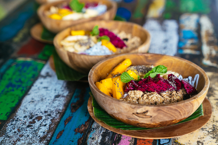 Close up smoothie bowl made with mango, banana, granola, grated coconut, dragon fruit, chia seeds and mint on colored background.の写真素材