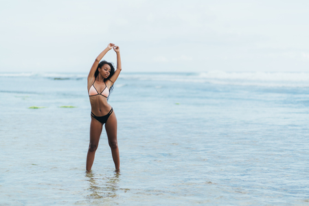 Beautiful dark skinned girl in swimwear resting on beach. African american model posing on tropical islandの写真素材