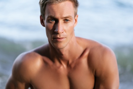 Portrait of sexy muscular man with bare-chested posing on camera at beachの写真素材