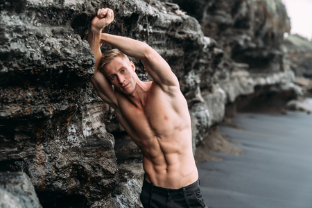 Sexy fitness male model in black pants and shirtless posing on black sandy beach.の写真素材