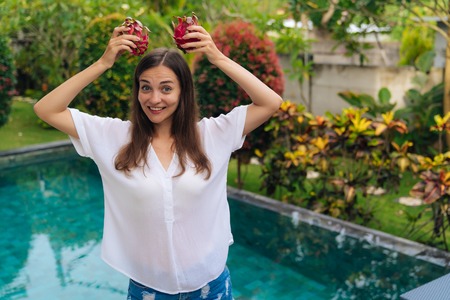 Portrait of funny girl has joyful expression and holds two dragon fruits over headの写真素材