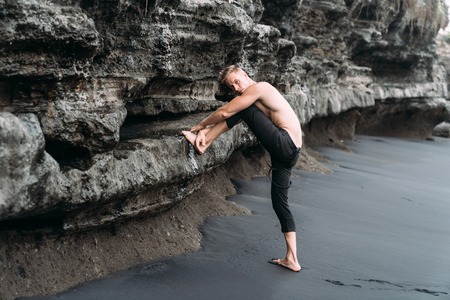 Sexy fitness male model in black pants and shirtless posing on black sandy beach.の写真素材