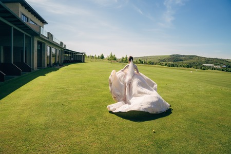 Backside view, bride runs in white wedding dress with veil on green fieldの写真素材