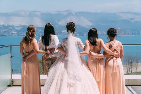 Backside view bride in white dress and girlfriends hold hands on balconyの写真素材