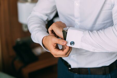 Close-up groom hands puts on cufflinks. Elegant gentleman clothers, white shirtの写真素材