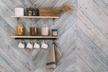 Cereals in glass jars on shelf, white cups, towel hang on hooks on kitchen wallの写真素材