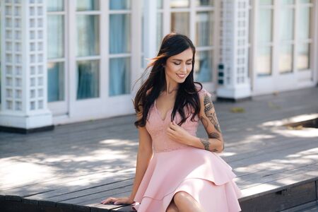 Beautiful smiling girl in pink dress sitting on wooden steps of street cafeの写真素材