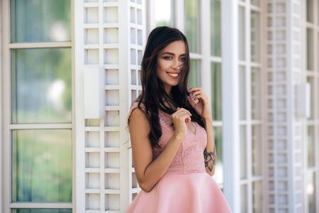 Cute model with beautiful smile in pink dress posing in street cafeの写真素材