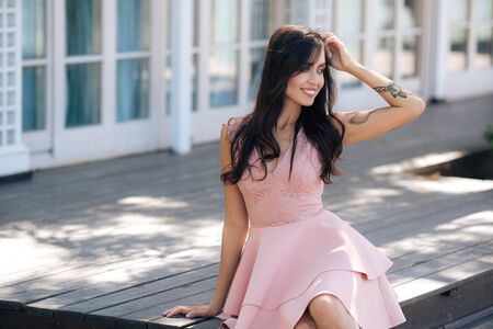 Beautiful sexy girl in pink dress sitting on wooden steps of street cafeの写真素材