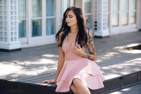 Beautiful sexy girl in pink dress sitting on wooden steps of street cafeの写真素材