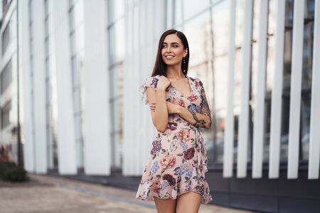 Beautiful happy young woman in colored dress posing near business centerの写真素材
