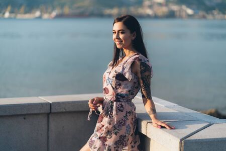 Beautiful smiling girl in summer dress posing in sunset time on waterfrontの写真素材