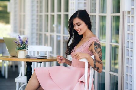 Beautiful brunette girl with beautiful smile in pink dress sits in street cafeの写真素材