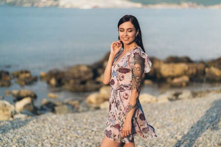 Beautiful smiling girl in summer dress posing in sunset time on waterfrontの写真素材
