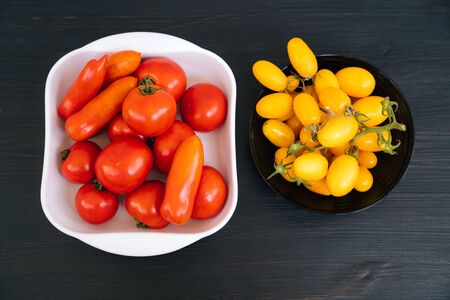 Top view of yellow, red cherry tomatoes in black, white bowl on dark backgroundの写真素材