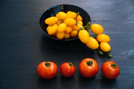 Top view of yellow and red cherry tomatoes in bowl on black wooden backgroundの写真素材