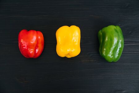 Top view of red, yellow, green bell peppers on black wooden backgroundの写真素材