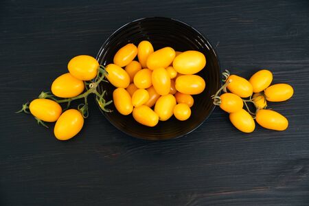 Top view, yellow cherry tomatoes in bowl on black wooden background, copy spaceの写真素材