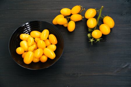 Top view, yellow cherry tomatoes in bowl on black wooden background, copy spaceの写真素材