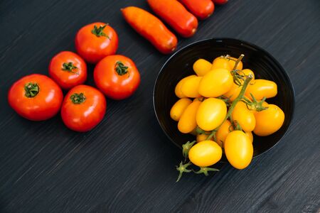 Top view of yellow and red cherry tomatoes in bowl on black wooden backgroundの写真素材